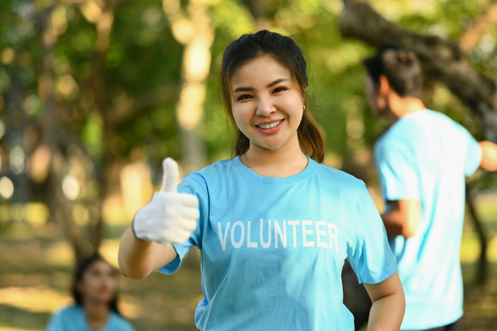 Beautiful Asian female activist in volunteer t-shirt showing thumbs up standing outdoor